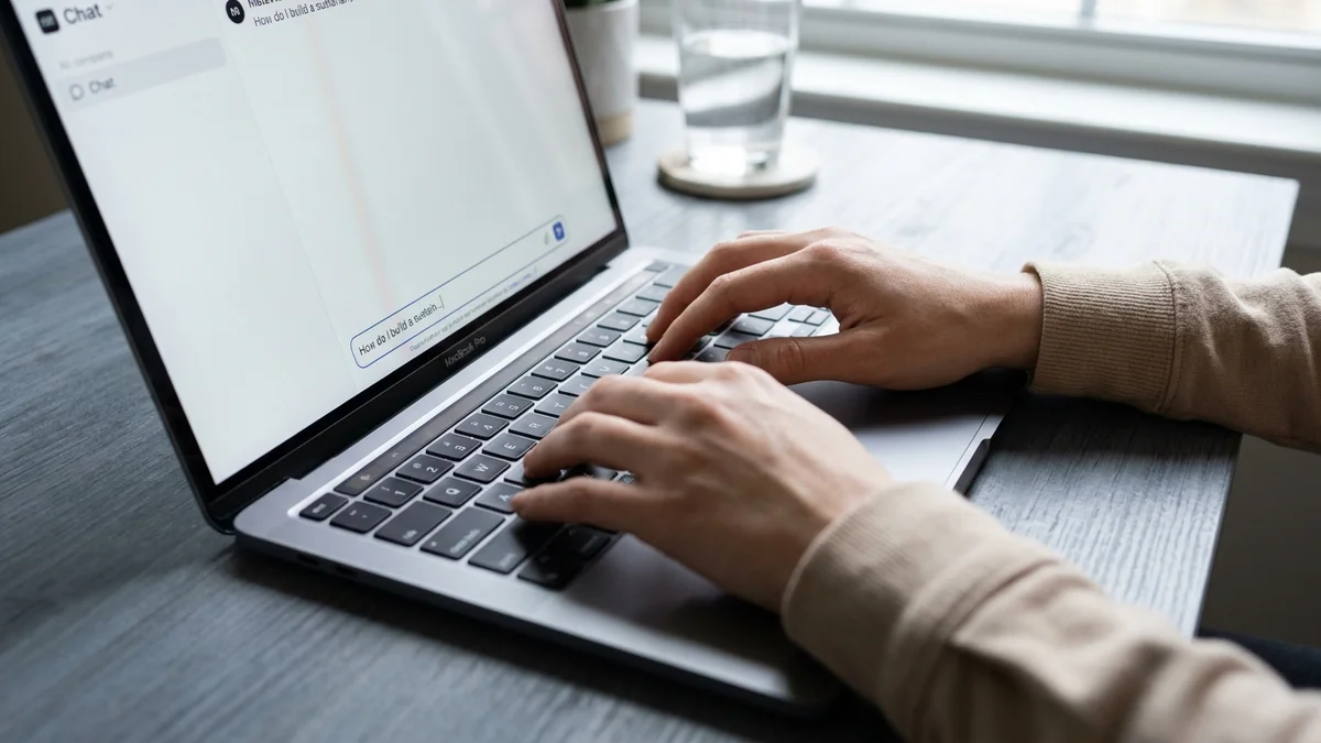 Hands typing on a MacBook with an AI chat interface on screen