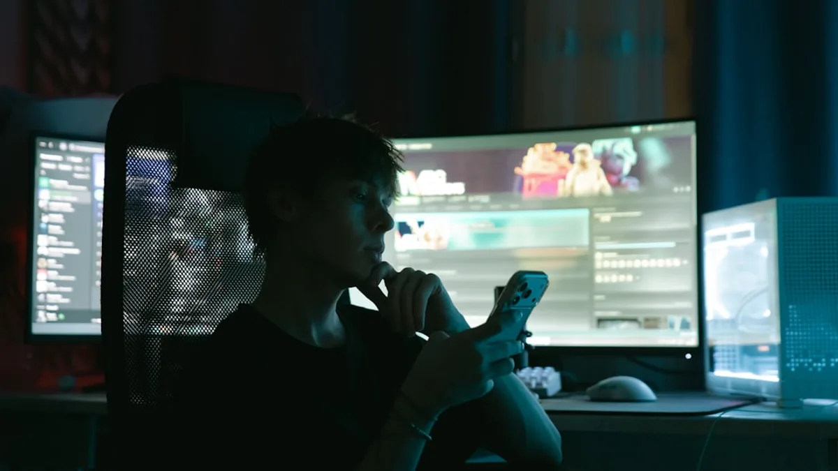Person looking at phone in front of multiple computer monitors