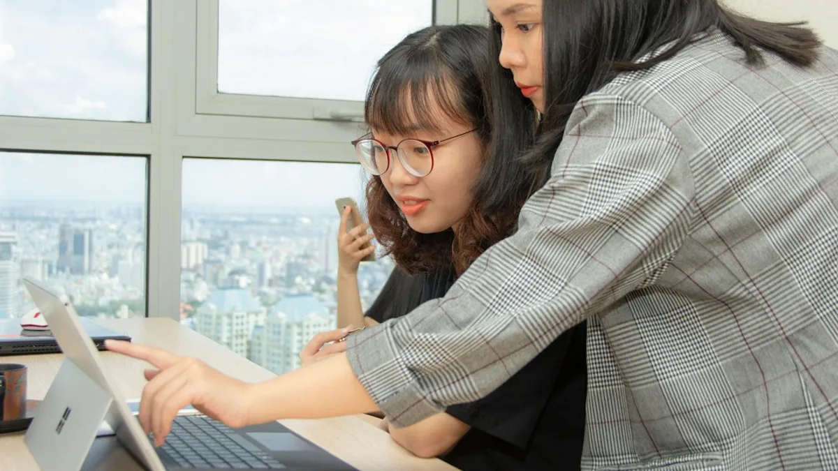 woman standing behind sitting woman in front of laptop computer