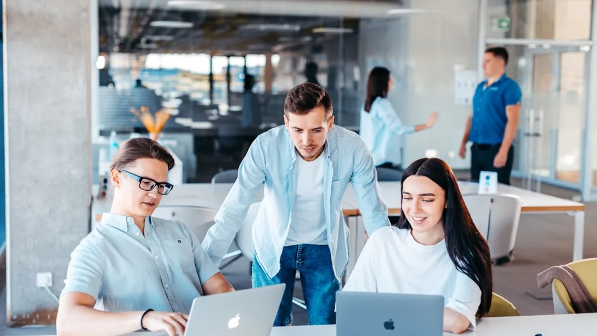 a group of people sitting around a table with laptops