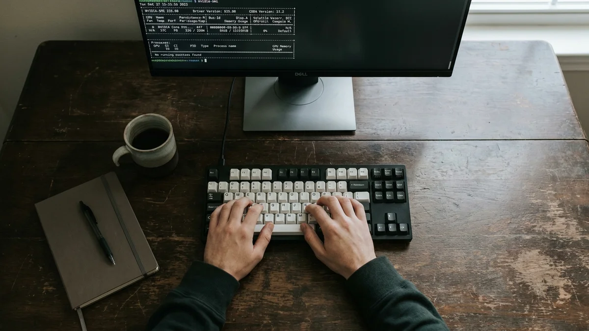 Developer hands typing while monitor shows nvidia-smi GPU memory output